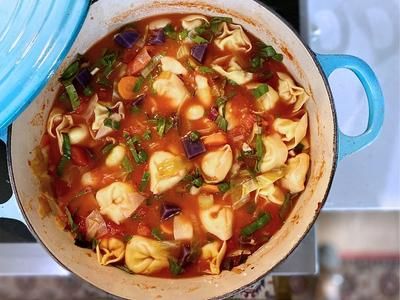 photo of a well-rounded dinner idea: a large dutch oven with lid to side showcasing minestrone soup with tortellini, carrots, lima beans, swiss chard and purple potatoes