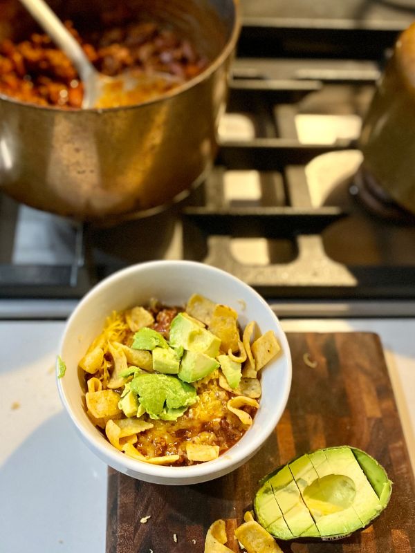 texas chili recipe with beans image for texas chili with beans recipe showing a top down view of a bowl of turkey chili topped with cheese fritos and avocados, next to a pot of chili on the stove