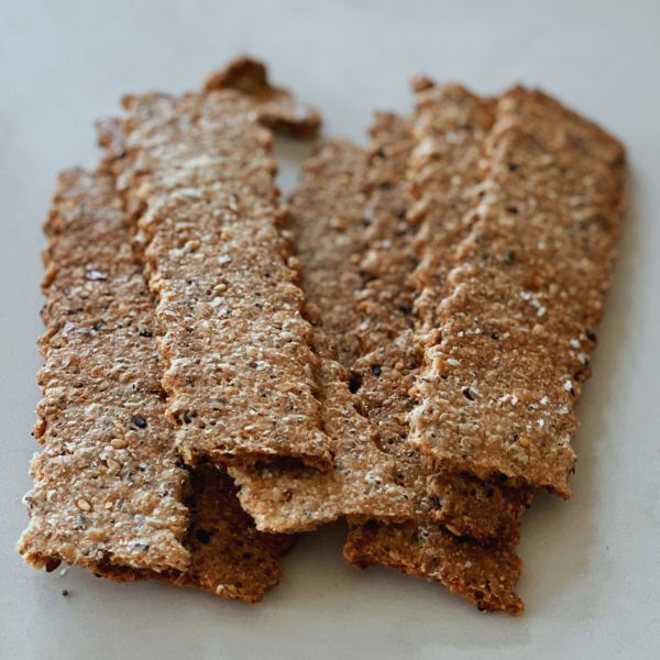 close up of crispy seeded sourdough crackers piled on a countertop topped with flaky salt