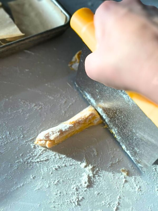 cutting pumpkin gnocchi top down view of sourdough pumpkin gnocchi dough rolled into a log being cut with a pastry cutter