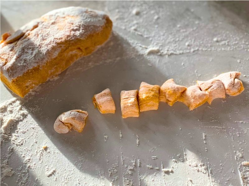 sourdough pumpkin gnocchi view of rested homemade gnocchi with pumpkin dough dusted in flour, and being cut